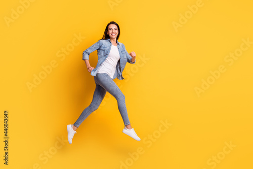 Full size profile portrait of pretty carefree girl running look camera beaming smile isolated on yellow color background