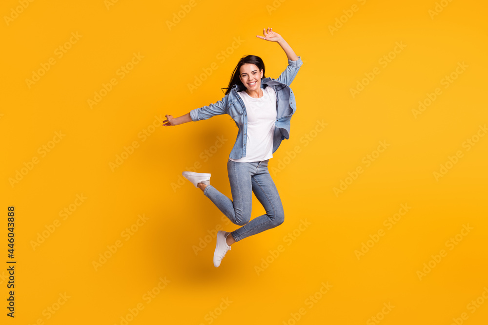Full size profile photo of cool optimistic brunette lady jump wear blue shirt jeans sneakers isolated on yellow background