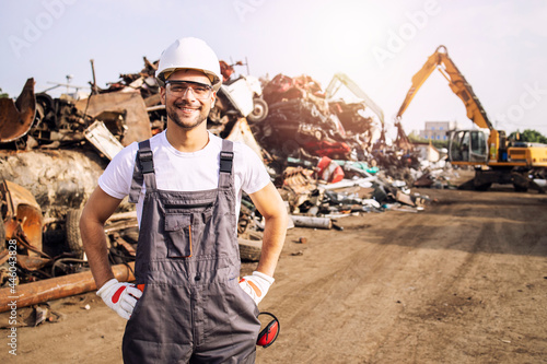 Portrait of worker standing in metal junk yard with crane lifting scrap metal for recycling. photo