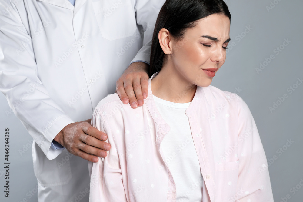 Doctor examining woman with shoulder pain on grey background Doctor examining woman with shoulder pain on grey background