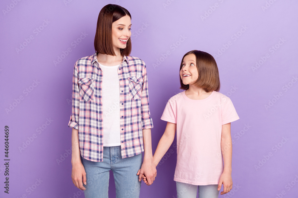 Portrait of two attractive cheerful girls mom daughter best friends holding hands isolated over purple violet color background Portrait of two attractive cheerful girls mom daughter best friends holding hands isolated over purple violet color background