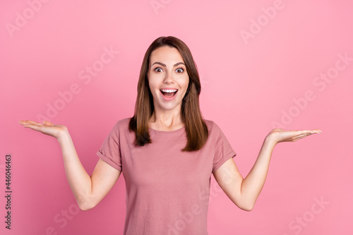 Photo of impressed brunette millennial lady hold empty space wear t-shirt isolated on pink color background © deagreez