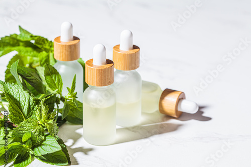 Mint essential oil in glass bottles, white marble background. Skin and body care concept.