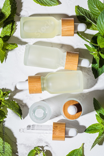 Mint essential oil in glass bottles, white marble background. Skin and body care concept. photo