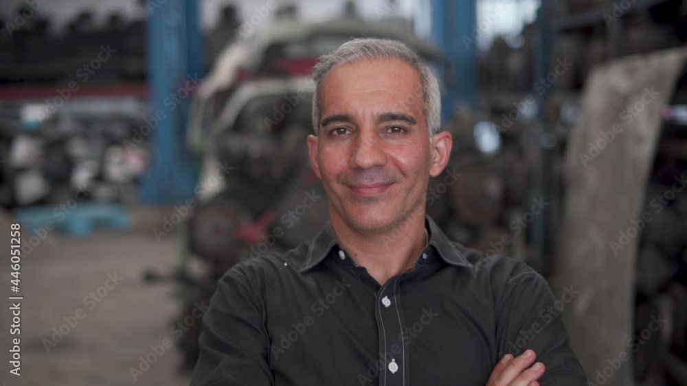 confident senior entrepreneur sitting on desk arms crossed smiling with computer laptop looking at camera in warehouse of old used car engine . happy old businessman owner start up at garage store confident senior entrepreneur sitting on desk arms crossed smiling with computer laptop looking at camera in warehouse of old used car engine . happy old businessman owner start up at garage store