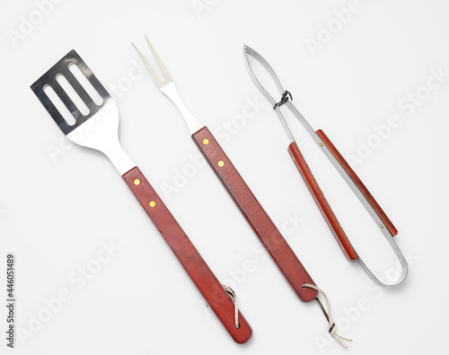 фотографія tongs, metal spatula and a fork with a wooden handle on a white background