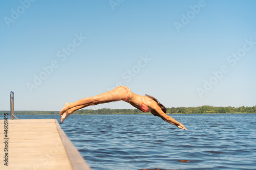 Fotografie Woman jumping into the lake from wooden pier