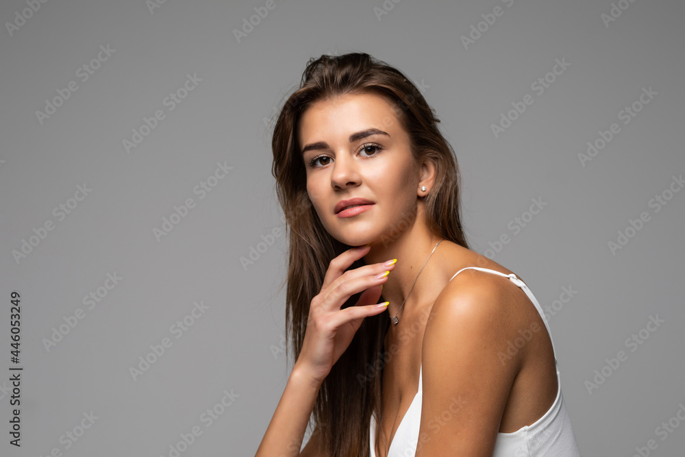 Naklejka premium Beautiful smiling girl with clean skin, natural make-up, and white teeth on grey background