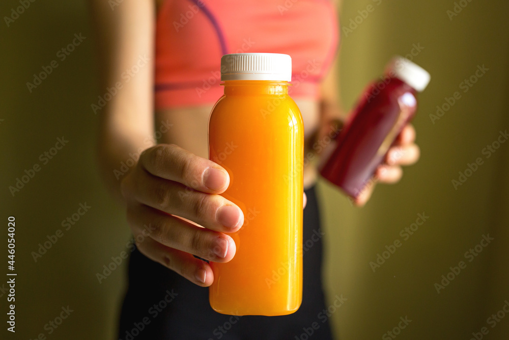 A female athlete holds bottles of freshly squeezed orange juice and vegetable juice in her hands. The concept of a healthy lifestyle, a healthy body.
