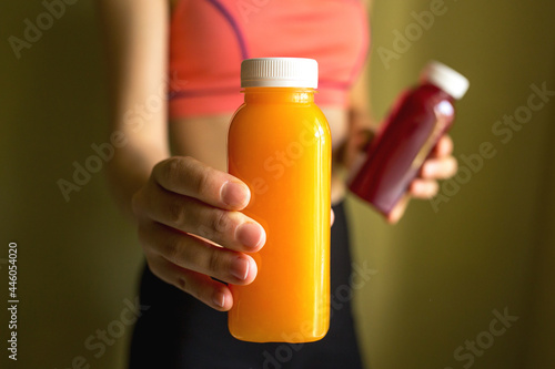 Obraz na płótnie A female athlete holds bottles of freshly squeezed orange juice and vegetable juice in her hands. The concept of a healthy lifestyle, a healthy body. w salonie