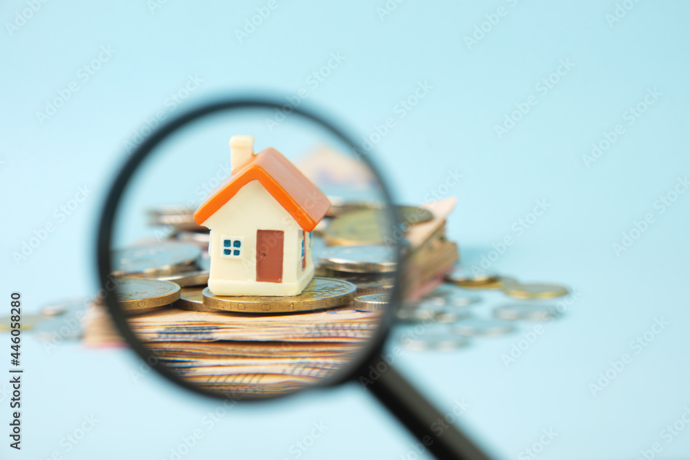 Miniature house and money under a magnifying glass. Concept of real estate investment, mortgage, home insurance, home purchase and sale. - obrazy, fototapety, plakaty 