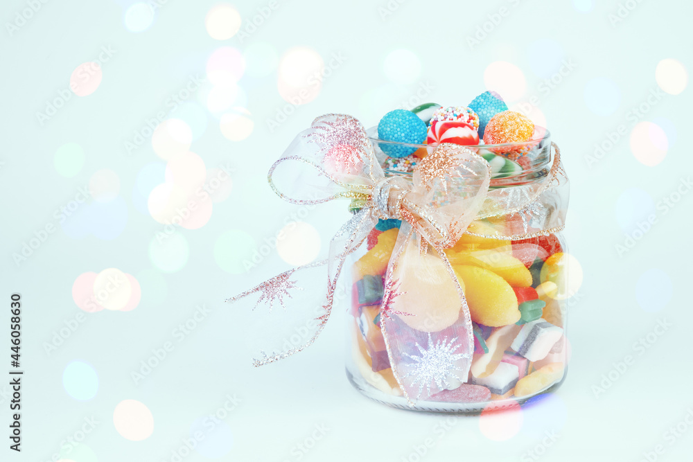 Jar of various sweets decorated with a bow. Glowing lights on the background. Festive concept.