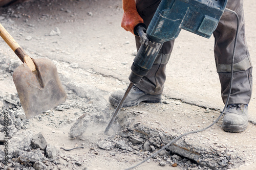 A worker repairs the road surface with a jackhammer on a summer day. Construction works on the road. Industrial background.