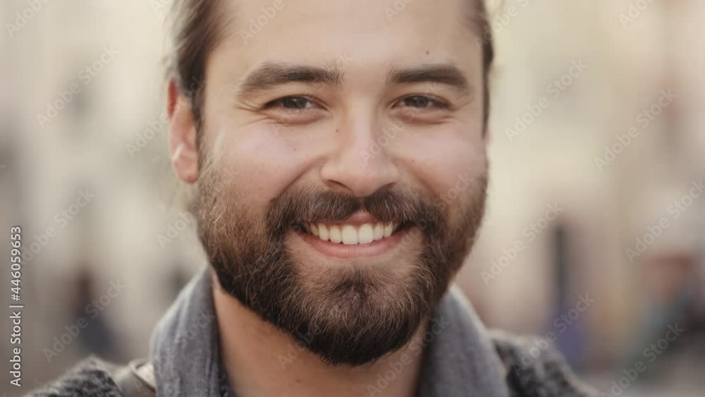 Portrait of a bearded happy man who is looking at the camera and smiling. His hair is swaying in the wind. Old town center in the background. 4K Portrait of a bearded happy man who is looking at the camera and smiling. His hair is swaying in the wind. Old town center in the background. 4K