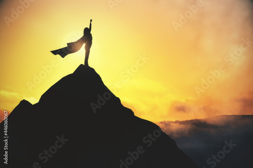 Success and satisfaction concept with super woman in waving coat on top of dark rock on yellow foggy sky background. photo