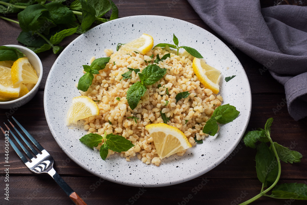 Boiled bulgur with fresh lemon and mint on a plate. A traditional oriental dish called Tabouleh. dark wooden background.