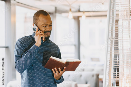 Man sitting in a cafe and talking on the phone, holding a notebook.