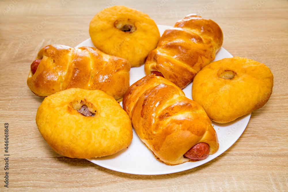 Belyashi with meat and sausages in a delicious yellow dough on a white round plate on a wooden board background. Bakery products national traditional dishes and pastries. Belyashi with meat and sausages in a delicious yellow dough on a white round plate on a wooden board background. Bakery products national traditional dishes and pastries.