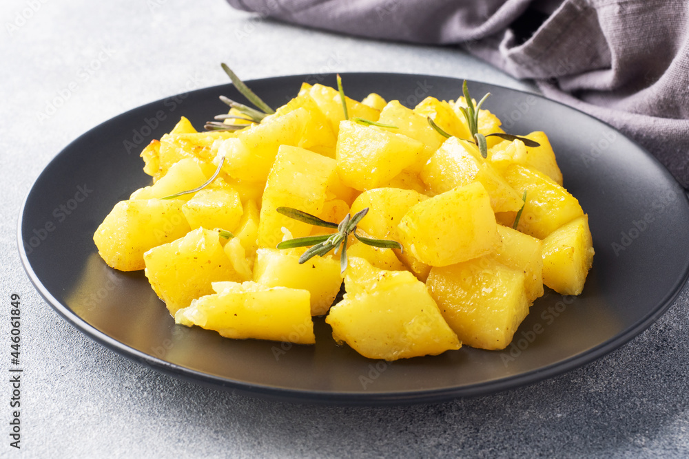 Delicious baked potatoes with spices cheese and rosemary on a black ceramic plate, a gray concrete background, copy space. Delicious baked potatoes with spices cheese and rosemary on a black ceramic plate, a gray concrete background, copy space.