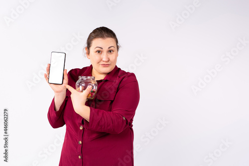 A beautiful overweight woman shows her mobile phone holding in the other hand a jar of colorful sweets. photo