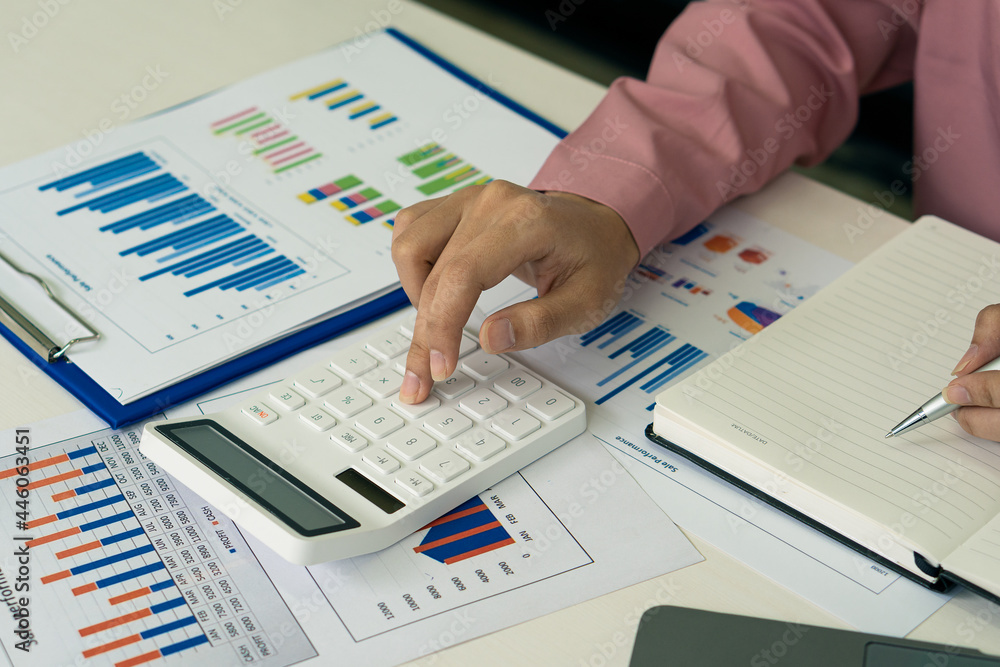 a businessman working in the office with a laptop and a desk graph data sheet with a calculator to calculate and analyze. a businessman working in the office with a laptop and a desk graph data sheet with a calculator to calculate and analyze.