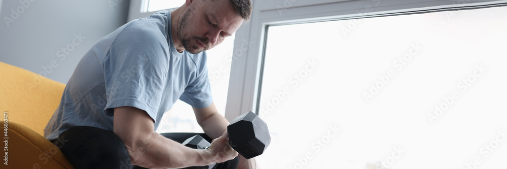 Young man sitting on chair and lifting dumbbell Young man sitting on chair and lifting dumbbell