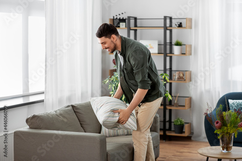 household, home improvement and cleaning concept - happy smiling man arranging cushions on sofa