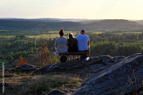 Three friends sitting on edge of mountain at sunset