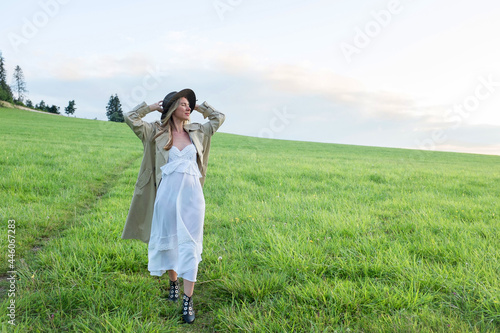 Happy woman enjoying sunset stay on the green grass on the forest peak of mountain. Fresh air, Travel, Summer, Holidays. Health care, authenticity, sense of balance and calmness.