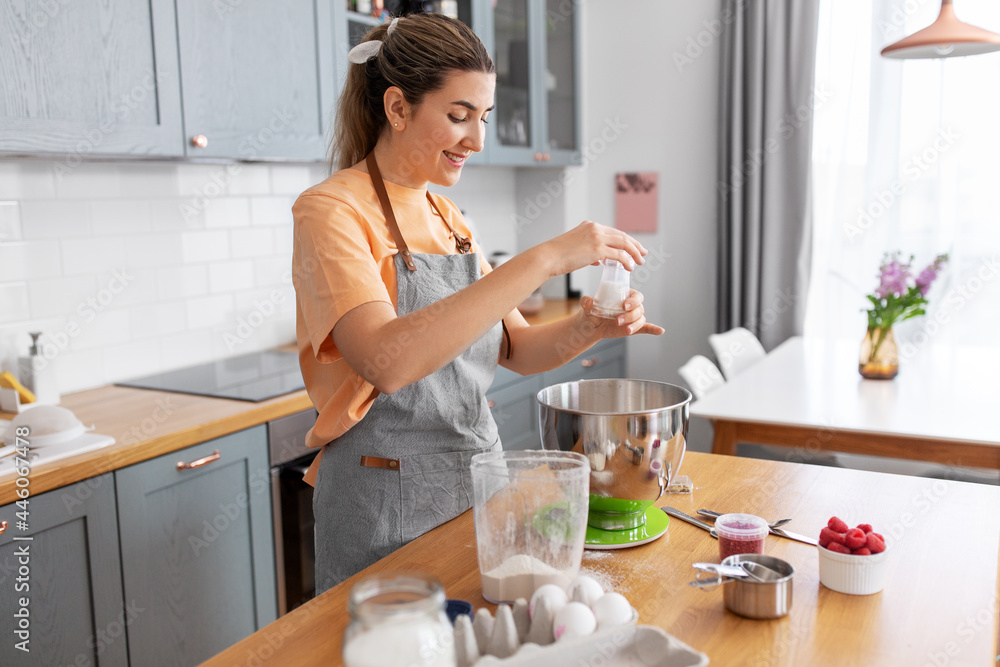 culinary, baking and people concept - happy smiling young woman cooking food on kitchen at home and adding salt culinary, baking and people concept - happy smiling young woman cooking food on kitchen at home and adding salt