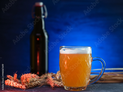 A mug of cold unfiltered wheat beer on a dark background with a blue backlight. Bugel bottle photo