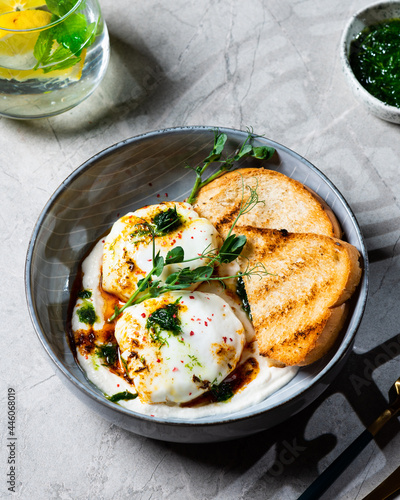 Cilbir or Turkish Eggs. dish served as mezze: poached eggs topped over herbed greek yogurt, then drizzled with hot spiced paprika olive oil. Turkish breakfast in a grey bowl on marble background