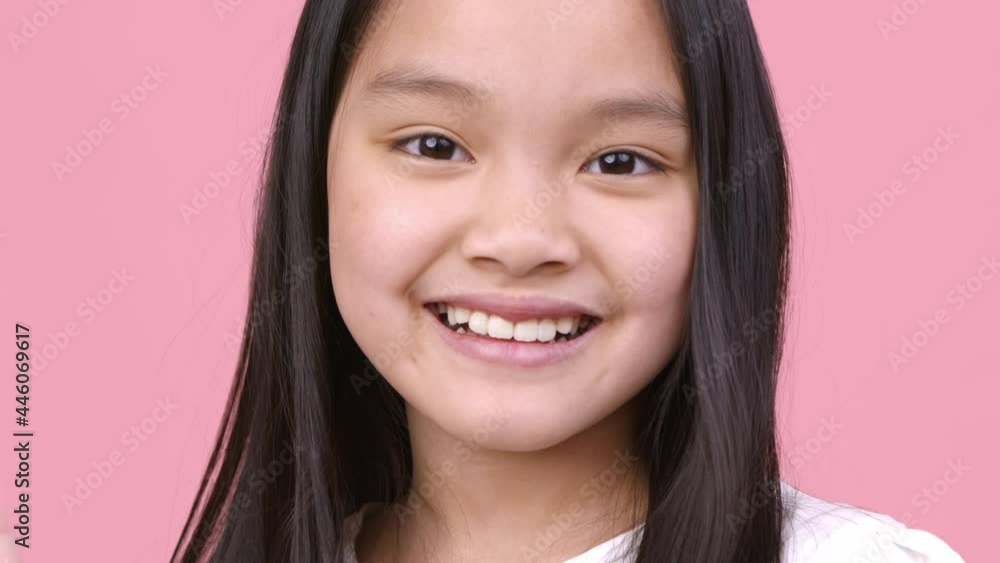 Cheerful greeting. Positive little asian girl waving hand hello and smiling to camera, pink studio background, close up Cheerful greeting. Positive little asian girl waving hand hello and smiling to camera, pink studio background, close up