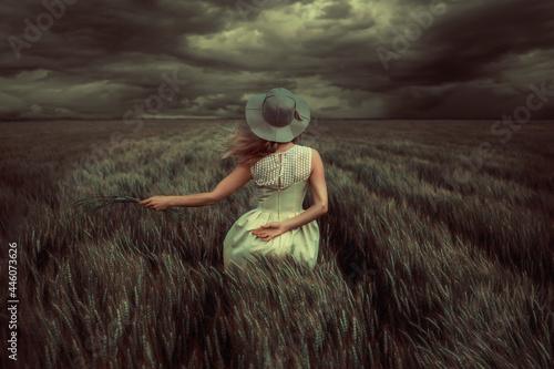 Foto Young blonde woman standing in a wheat field, wearing a yellow summer dress, on