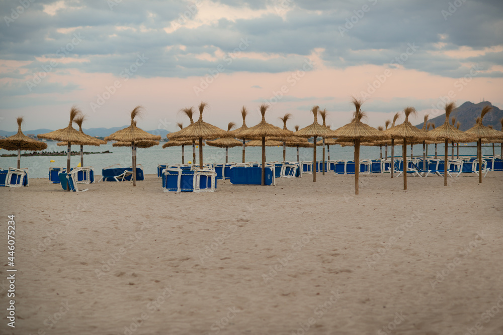 Empty Sun Loungers and Straw Umbrellas on a Beach in Mallorca in the Balearic Islands