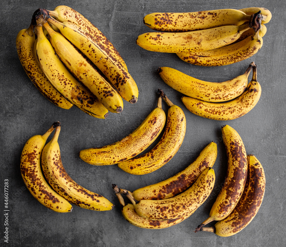 Ripe bananas on dark concrete background. A bunch of organic bananas ready to eat. Yellow and orange bananas with dark spots for vegan smoothies and dessert recipes. Ripe bananas on dark concrete background. A bunch of organic bananas ready to eat. Yellow and orange bananas with dark spots for vegan smoothies and dessert recipes.