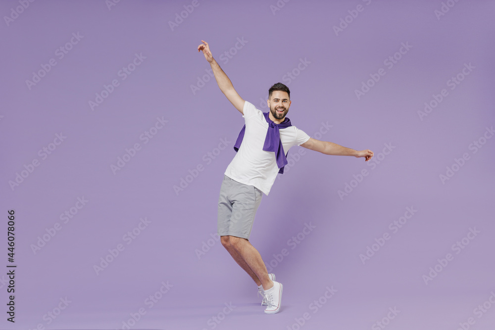 Full size body length joyful fun young brunet man 20s wear white t-shirt purple shirt standing on toes dancing lean back have fun spreading hands isolated on pastel violet background studio portrait