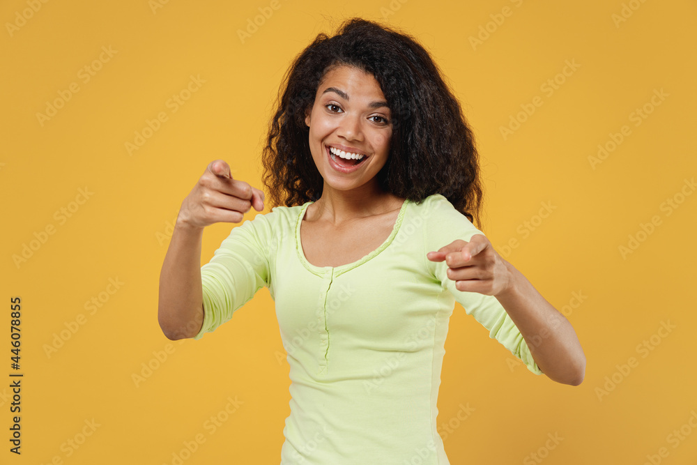 Fun joyful african american young woman 20s wear green shirt pointing index fingers camera on you motivating encourage isolated on yellow background studio portrait. People emotions lifestyle concept Fun joyful african american young woman 20s wear green shirt pointing index fingers camera on you motivating encourage isolated on yellow background studio portrait. People emotions lifestyle concept