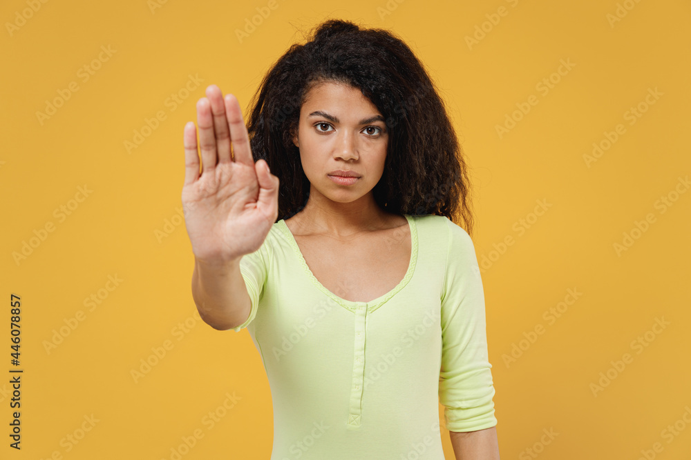 Serious pensive embarrassed african american young brunette woman 20s wears green shirt showing stop gesture with palm isolated on yellow background studio portrait. People emotions lifestyle concept Serious pensive embarrassed african american young brunette woman 20s wears green shirt showing stop gesture with palm isolated on yellow background studio portrait. People emotions lifestyle concept