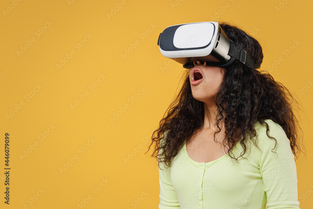 Surprised shocked amazed astonished african american young woman 20s wear green shirt watching in vr headset pc gadget isolated on yellow background studio portrait. People emotions lifestyle concept Surprised shocked amazed astonished african american young woman 20s wear green shirt watching in vr headset pc gadget isolated on yellow background studio portrait. People emotions lifestyle concept