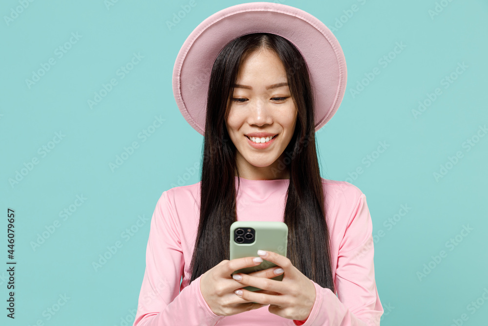 Pleased brunette asian woman 20s wear pink clothes hold in hand using mobile cell phone chatting browsing send sms to friend read news try to find information isolated on pastel blue color background Pleased brunette asian woman 20s wear pink clothes hold in hand using mobile cell phone chatting browsing send sms to friend read news try to find information isolated on pastel blue color background