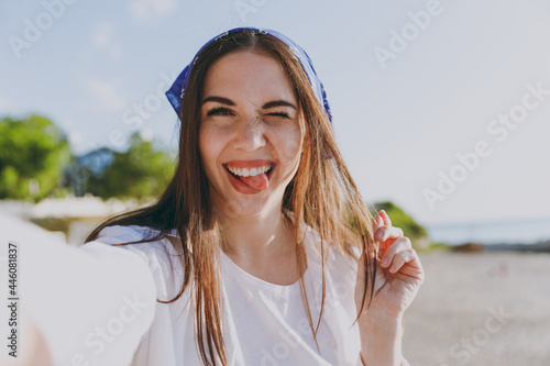Close up cute young traveler tourist woman 20s in blue bandana shirt summer casual clothes rest do selfie shot mobile cell phone blink outdoors at sea beach People vacation lifestyle journey concept.