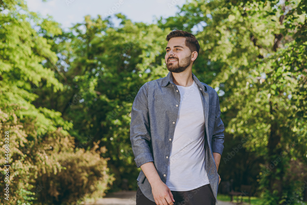 Young happy calm minded smiling man 20s wear blue casual shirt walk try look aside rest relax in spring green city park go down alley sunshine lawn outdoors on nature Urban lifestyle leisure concept. Young happy calm minded smiling man 20s wear blue casual shirt walk try look aside rest relax in spring green city park go down alley sunshine lawn outdoors on nature Urban lifestyle leisure concept.
