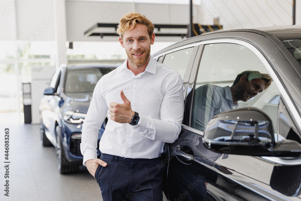 Man customer male buyer businessman client in white shirt chooses auto show thumb up wants to buy new automobile in car showroom vehicle salon dealership store motor show indoor. Car sales concept Man customer male buyer businessman client in white shirt chooses auto show thumb up wants to buy new automobile in car showroom vehicle salon dealership store motor show indoor. Car sales concept