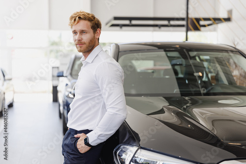 Confident pensive man customer buyer businessman client wears white shirt chooses auto wants to buy new automobile in car showroom vehicle salon dealership store motor show indoor. Car sales concept