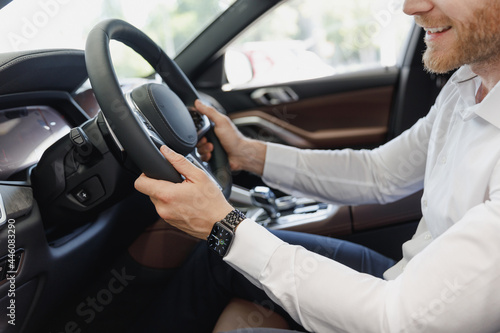 Close up cropped up photo shot customer buyer businessman client man 20s wearing white shirt watch sitting in car salon hold steering wheel driving automobile modern vehicle Car sales driver concept.