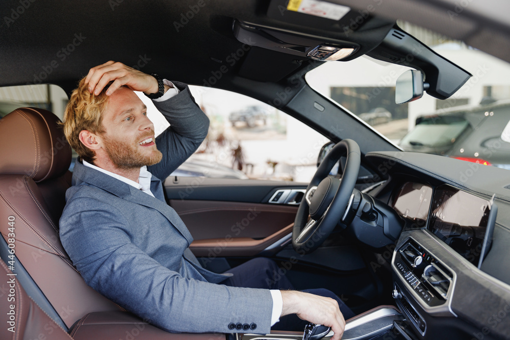 Side view happy man driver male cabdriver wearing classic grey suit drive car hold wheel touch haircut look at mirror in traffic jam test auto want buy new automobile vehicle Sale transport concept. Side view happy man driver male cabdriver wearing classic grey suit drive car hold wheel touch haircut look at mirror in traffic jam test auto want buy new automobile vehicle Sale transport concept.