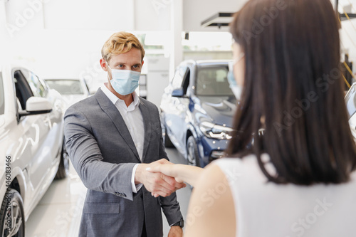 Man customer male client buyer in classic suit pandemic mask choose auto want buy new car automobile consult with salesman shake hand in showroom salon dealership store motor show indoor Sale concept