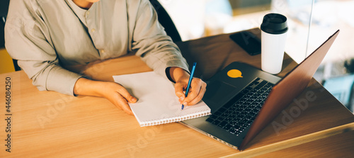 A woman in glasses studying online with her laptop, writing in notepad. Easy online education with computer and eLearning webinars concept