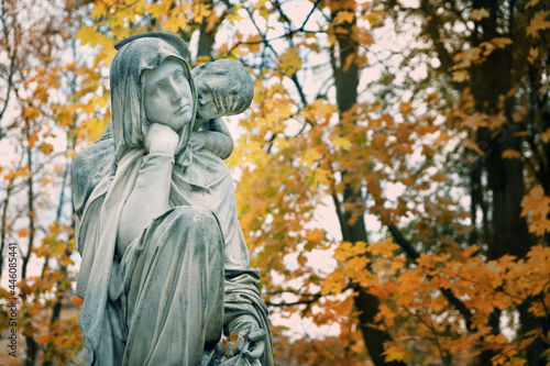 Old cemetery monument of sad mother and baby angel, autumn background. Beautiful grieving woman gravestone. concept of mourning, condolence, Remember, mourn, memory